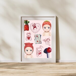 May include: A framed print featuring a collection of whimsical illustrations and figurines. The artwork includes a strawberry-themed doll, a teddy bear, playing cards, and a cherub. The color palette is primarily pink and red.