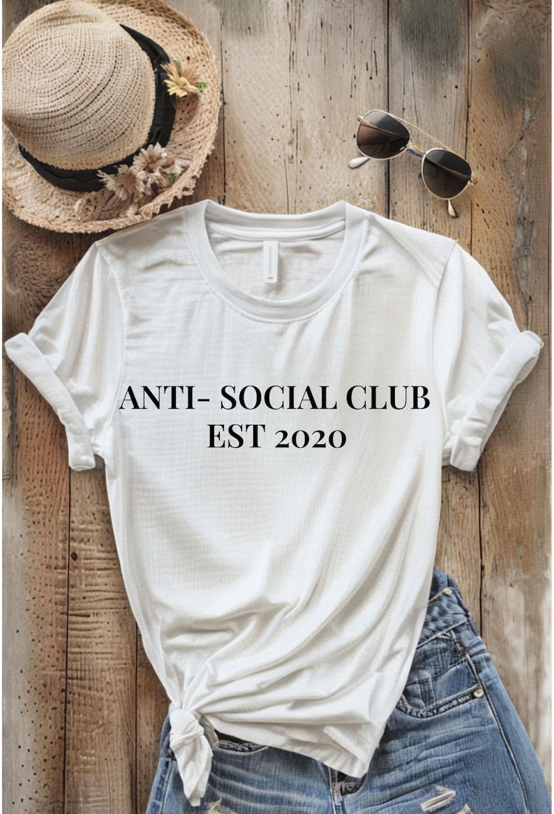 White tee on a wood background with the words anti-social club est. 2020