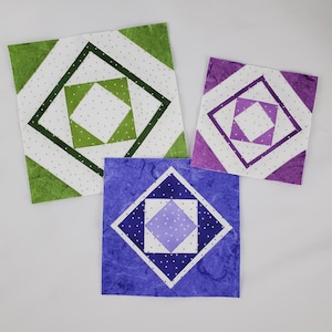 May include: Three fabric squares with a geometric pattern. The squares are in shades of green, purple, and blue. The pattern is a series of overlapping squares with white polka dots.