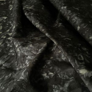 May include: A close-up of a fabric with a marbled pattern. The fabric is primarily black with white and gray swirls and patches. The fabric is folded, showing the texture and depth of the material.