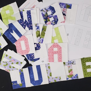 Peut inclure: Un ensemble de carrés de tissu avec des lettres imprimées dessus. Les lettres épellent le mot "JULIE". Les carrés sont de différentes couleurs et motifs, notamment bleu, vert, rose et blanc.