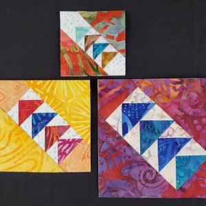 May include: Three fabric squares with a patchwork design featuring a pattern of white, red, blue, and yellow triangles. The squares are different sizes and are arranged in a vertical row.