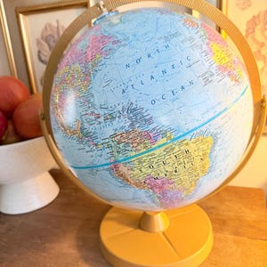 May include: A vintage-style globe with a light blue ocean and colorful landmasses. The globe is mounted on a yellow base and supported by a matching meridian ring. The globe is a decorative educational item.