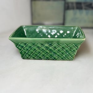 May include: A rectangular ceramic bowl with a glossy emerald green glaze. The exterior features a raised, diamond-shaped lattice pattern that resembles woven basketry. The rim is smooth and flat, framing the deep, open interior of the vessel.