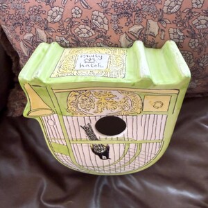 May include: A decorative birdhouse in a unique carriage shape, painted in light green and cream. The birdhouse features a black bird illustration, a round entry hole, and the text "molly hatch".