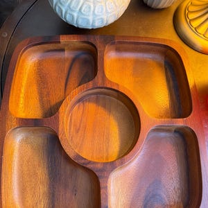 May include: A vintage wooden serving tray with five compartments. The tray has a warm, reddish-brown hue and a smooth finish. The compartments include four rectangular sections and a central circular area, ideal for serving snacks or appetizers.