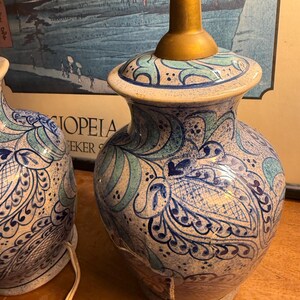 May include: A pair of ceramic table lamps with a blue and white floral design. The lamps have a brass-colored base and a decorative pattern. The lamps are on a wooden surface.