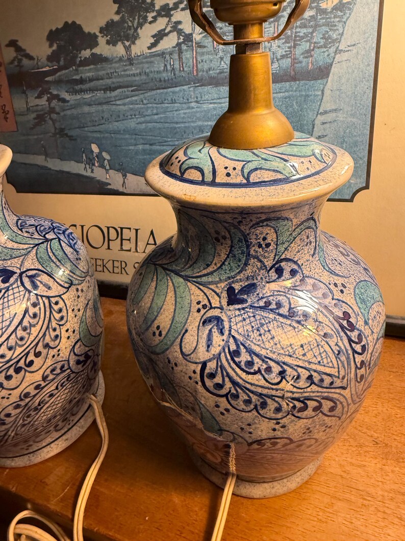 May include: A pair of ceramic table lamps with a blue and white floral design. The lamps have a brass-colored base and a decorative pattern. The lamps are on a wooden surface.