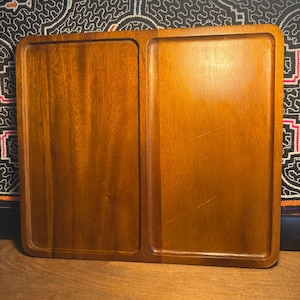 May include: A rectangular wooden serving tray with two distinct compartments. The tray is made of a warm-toned wood, likely mahogany or a similar species, and has a smooth, polished finish. The design is simple and functional, suitable for serving appetizers or small dishes.