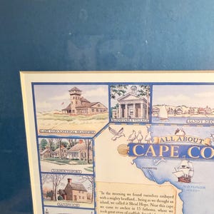 May include: A framed watercolor map titled "All About Cape Cod" featuring illustrations of landmarks and historical text. The map includes images of buildings, a bridge, and a sailing ship, with text describing the area's history.