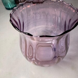 Peut inclure: Un vase d&eacute;coratif en verre violet clair avec un bord festonn&eacute;. Le vase a un corps arrondi et une ouverture l&eacute;g&egrave;rement &eacute;vas&eacute;e. Le verre a un aspect textur&eacute; et le bord est d'une teinte violette plus fonc&eacute;e.