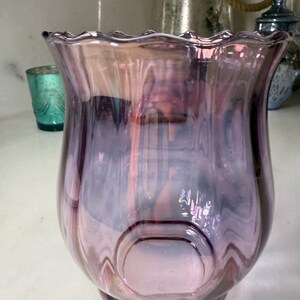 Peut inclure: Un vase d&eacute;coratif en verre aux tons violets et roses. Le vase a un bord &eacute;vas&eacute; et ondul&eacute; et un corps arrondi avec une indentation circulaire. Le verre a une finition brillante, refl&eacute;tant la lumi&egrave;re. Le vase est probablement utilis&eacute; pour la d&eacute;coration int&eacute;rieure.