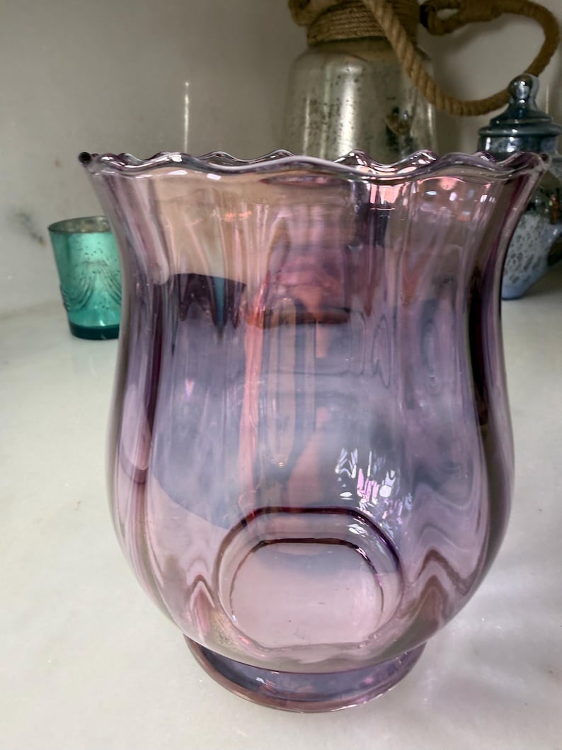 Peut inclure: Un vase d&eacute;coratif en verre aux tons violets et roses. Le vase a un bord &eacute;vas&eacute; et ondul&eacute; et un corps arrondi avec une indentation circulaire. Le verre a une finition brillante, refl&eacute;tant la lumi&egrave;re. Le vase est probablement utilis&eacute; pour la d&eacute;coration int&eacute;rieure.