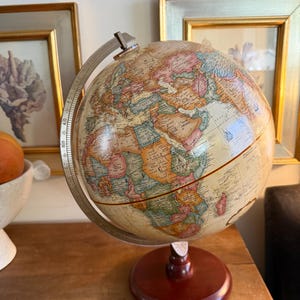 May include: A vintage-style globe with a detailed map of the world. The globe features a cream-colored sphere with colorful continents and countries. It is mounted on a dark brown wooden base and has a metal meridian ring.