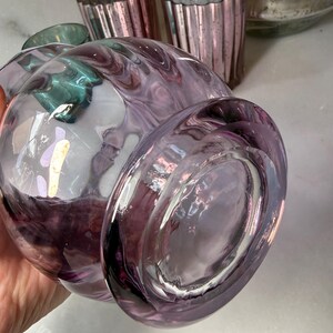 Peut inclure: Un grand vase en verre transparent avec un motif tourbillonnant et marbr&eacute; dans des tons de violet et de blanc. Plusieurs petits photophores en verre rose cannel&eacute; sont en arri&egrave;re-plan. Le vase a une forme arrondie et une base large.