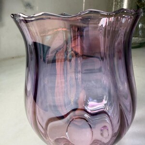 Peut inclure: Un vase d&eacute;coratif en verre violet iris&eacute; avec un bord festonn&eacute;. Le vase a un corps bulbeux et une ouverture &eacute;vas&eacute;e. Le verre pr&eacute;sente un motif tourbillonnant et une finition brillante, refl&eacute;tant la lumi&egrave;re et cr&eacute;ant un jeu de couleurs.