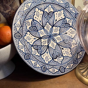 May include: A large, round ceramic plate with a detailed blue and white floral pattern. The plate features a central floral design surrounded by intricate border patterns. The plate is likely 12 inches in diameter.