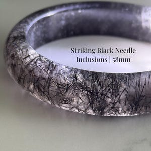 May include: A black rutilated quartz bangle featuring striking black needle inclusions. The text on the image reads Black Rutilated Quartz Bangle, Striking Black Needle Inclusions | 58mm, and AmorGemsBoutique. The bangle has a diameter of 58mm.
