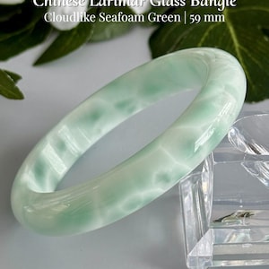 May include: A Chinese Larimar glass bangle in a cloudlike seafoam green color, measuring 59 mm. The text on the image reads: Chinese Larimar Glass Bangle, Cloudlike Seafoam Green | 59 mm, and AmorGemsBoutique.