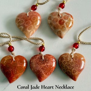 May include: Five heart-shaped pendants made of coral jade, each suspended on a braided beige cord with a single red bead accent. The text Coral Jade Heart Necklace, Choose Your Favorite, 5 One-of-a-Kind Hearts, and AmorGemsBoutique is visible.