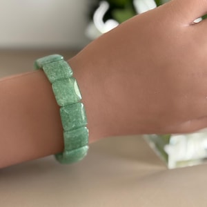 Pu&ograve; includere: Un braccialetto verde chiaro composto da perline quadrate. Il braccialetto &egrave; indossato su un polso. Le perline hanno un aspetto leggermente strutturato. Il braccialetto &egrave; un gioiello.