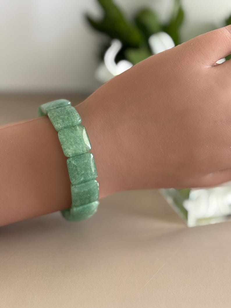 Pu&ograve; includere: Un braccialetto verde chiaro composto da perline quadrate. Il braccialetto &egrave; indossato su un polso. Le perline hanno un aspetto leggermente strutturato. Il braccialetto &egrave; un gioiello.
