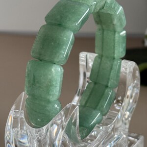 Pu&ograve; includere: Un braccialetto di avventurina verde con perline quadrate. Il braccialetto &egrave; esposto su un supporto trasparente e decorativo. Le perline hanno una superficie lucida e liscia e un aspetto traslucido. Il braccialetto &egrave; un gioiello.