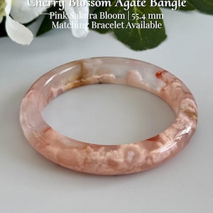 May include: A smooth, translucent cherry blossom agate bangle featuring soft pink and white floral-like inclusions. The bangle has an inner diameter of 55.4 mm. Text on the image reads: Cherry Blossom Agate Bangle, Pink Sakura Bloom, 55.4 mm, Matching Bracelet Available, AmorGemsBoutique.