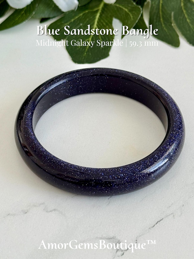 May include: A dark blue sandstone bangle with a glittery finish, featuring the text Blue Sandstone Bangle Midnight Galaxy Sparkle 59.3 mm and AmorGemsBoutique. The circular bracelet has a smooth, polished surface with embedded reflective particles.