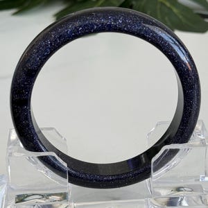 May include: A circular bangle bracelet crafted from dark blue sandstone, featuring a smooth, polished surface embedded with numerous tiny, reflective metallic flecks that create a shimmering, star-like appearance throughout the deep blue material.