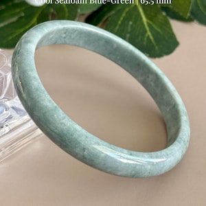 May include: A smooth, polished Grade A blue water jadeite bangle bracelet in a cool seafoam blue-green color. The text on the image reads: Certified Grade A Blue Water Jadeite, Cool Seafoam Blue-Green, 65.5 mm, and AmorGemsBoutique.