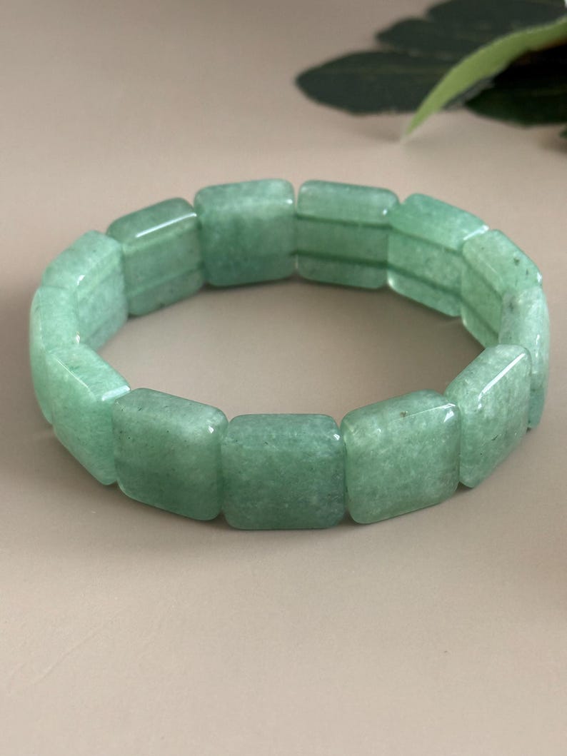 Pu&ograve; includere: Un braccialetto di avventurina verde. Il braccialetto &egrave; composto da perline rettangolari e lucide. Le perline sono di colore verde chiaro e hanno un aspetto leggermente traslucido. Il braccialetto &egrave; esposto su uno sfondo neutro.
