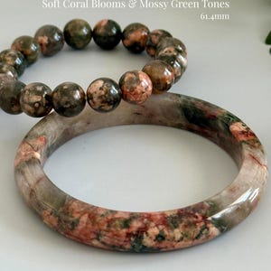 May include: Two bracelets made of Pink Sakura Agate with Green Rutile. One is a beaded bracelet, and the other is a bangle. The text on the image says "Soft Coral Blooms & Mossy Green Tones" and "61.4mm".