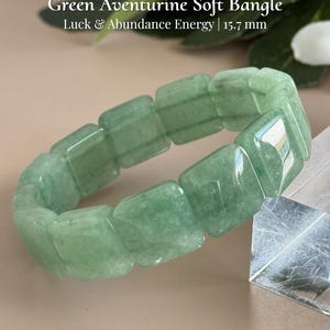 Pu&ograve; includere: Un bracciale morbido in avventurina verde composto da pietre rettangolari. Il testo sull'immagine recita "Green Aventurine Soft Bangle, Luck & Abundance Energy | 15.7 mm" e "AmorGemsBoutique". Il bracciale &egrave; di colore verde chiaro.