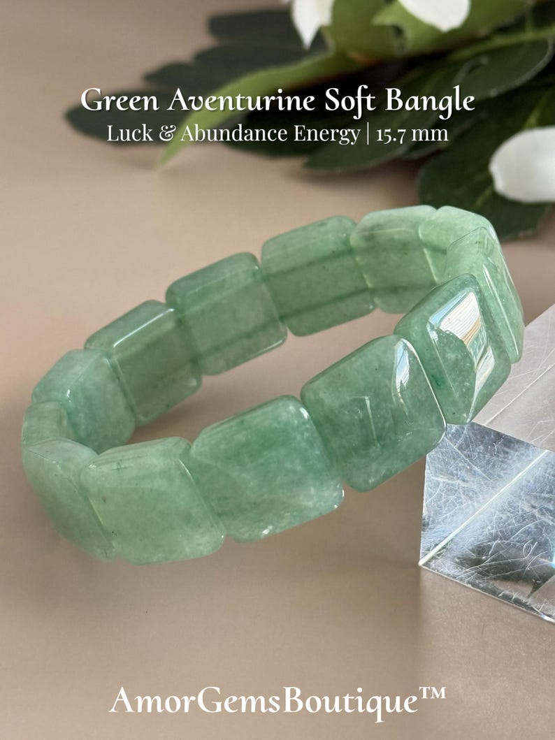 Pu&ograve; includere: Un bracciale morbido in avventurina verde composto da pietre rettangolari. Il testo sull'immagine recita "Green Aventurine Soft Bangle, Luck & Abundance Energy | 15.7 mm" e "AmorGemsBoutique". Il bracciale &egrave; di colore verde chiaro.