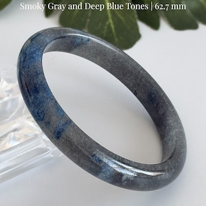 May include: A smooth, polished Blue Strawberry Quartz bangle bracelet featuring smoky gray and deep blue tones. The text on the image reads Blue Strawberry Quartz, Smoky Gray and Deep Blue Tones | 62.7 mm, and AmorGemsBoutique.
