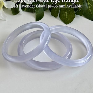 May include: Three smooth, lavender-colored cat eye bangles with a soft, translucent glow. The text on the image reads: Lavender Cat Eye Bangle, Soft Lavender Glow | 58-60 mm Available, and AmorGemsBoutique. The bangles have a rounded profile.