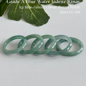 May include: Five Grade A blue water jadeite rings with a classic round profile and icy blue-green color. The text reads: Grade A Blue Water Jadeite Rings, Icy Blue-Green | Classic Round Profile, Sizes 6 1/2-8 7/8, and AmorGemsBoutique.