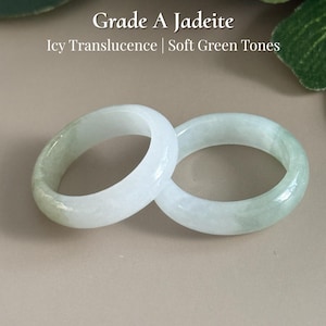 May include: Two jadeite rings with soft green tones and icy translucence. The rings are displayed on a neutral background with text that reads "Grade A Jadeite" and "AmorGems Boutique".