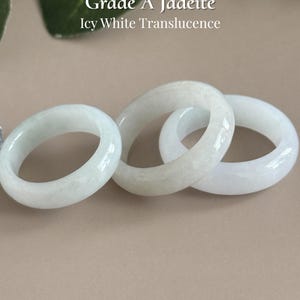 May include: Three smooth, circular rings crafted from Grade A jadeite with icy white translucence. The text Grade A Jadeite Icy White Translucence appears at the top, and the text AmorGemsBoutique appears at the bottom of the image.