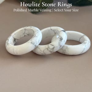 May include: Three Howlite stone rings with polished marble veining. The rings are white with gray marbling and are displayed on a neutral background. Text on the image reads "Howlite Stone Rings" and "Select Your Size".