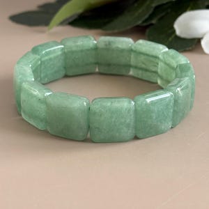 Pu&ograve; includere: Un braccialetto verde chiaro composto da pietre rettangolari lucide. Il braccialetto &egrave; di un colore verde tenue e sembra essere fatto di una pietra naturale. Il braccialetto ha una circonferenza di circa 18 cm.