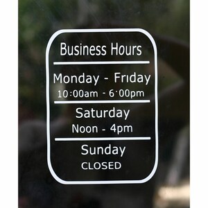 May include: A white sign with black text on a black background listing business hours. The sign says "Business Hours", "Monday - Friday 10:00am - 6:00pm", "Saturday Noon - 4pm", and "Sunday CLOSED".