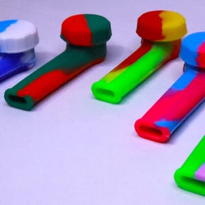 May include: Five colorful silicone pipes in blue, green, red, pink, and purple. Each pipe has a matching cap. The pipes are designed with a curved shape and a small opening at the end. The pipes are made of a flexible material.