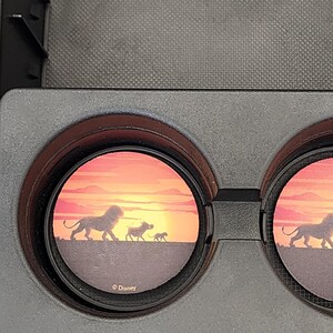 May include: Black car cup holder inserts featuring a sunset scene with silhouettes of lions, a warthog, and a cub. The design is reminiscent of the Lion King, with the Disney logo visible.