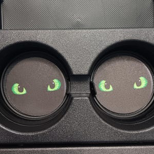 Puede incluir: Posavasos negros para portavasos de coche con diseño de ojos verdes. Los ojos tienen forma de media luna y son de color verde brillante. Los posavasos son redondos.