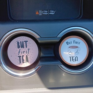May include: Two car coasters with the text "But First Tea". One coaster is pink with black dots and the text in white. The other coaster is white with a brown border and a teacup graphic.