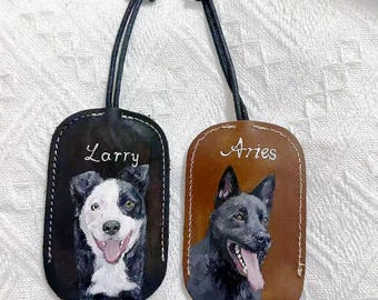 May include: Two leather keychains with dog portraits. One is black with a white and black dog and the name "Larry". The other is brown with a black dog and the name "Aries". Both have a black leather strap and a metal ring.