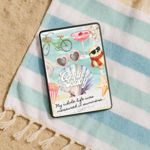 May include: A black tablet case with a summer design. The case features a bicycle, heart-shaped sunglasses, a teddy bear, and a seashell. Text includes "Connie Baby" and "My whole life was measured in summers..."