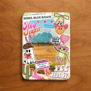 May include: A rectangular sticker with a western theme. It features a landscape with a ghost reading a book, a frog in cowboy boots, and text that says "Hey Sugar", "Yee Haw", and "I'd rather be at Rebel Blue Ranch".
